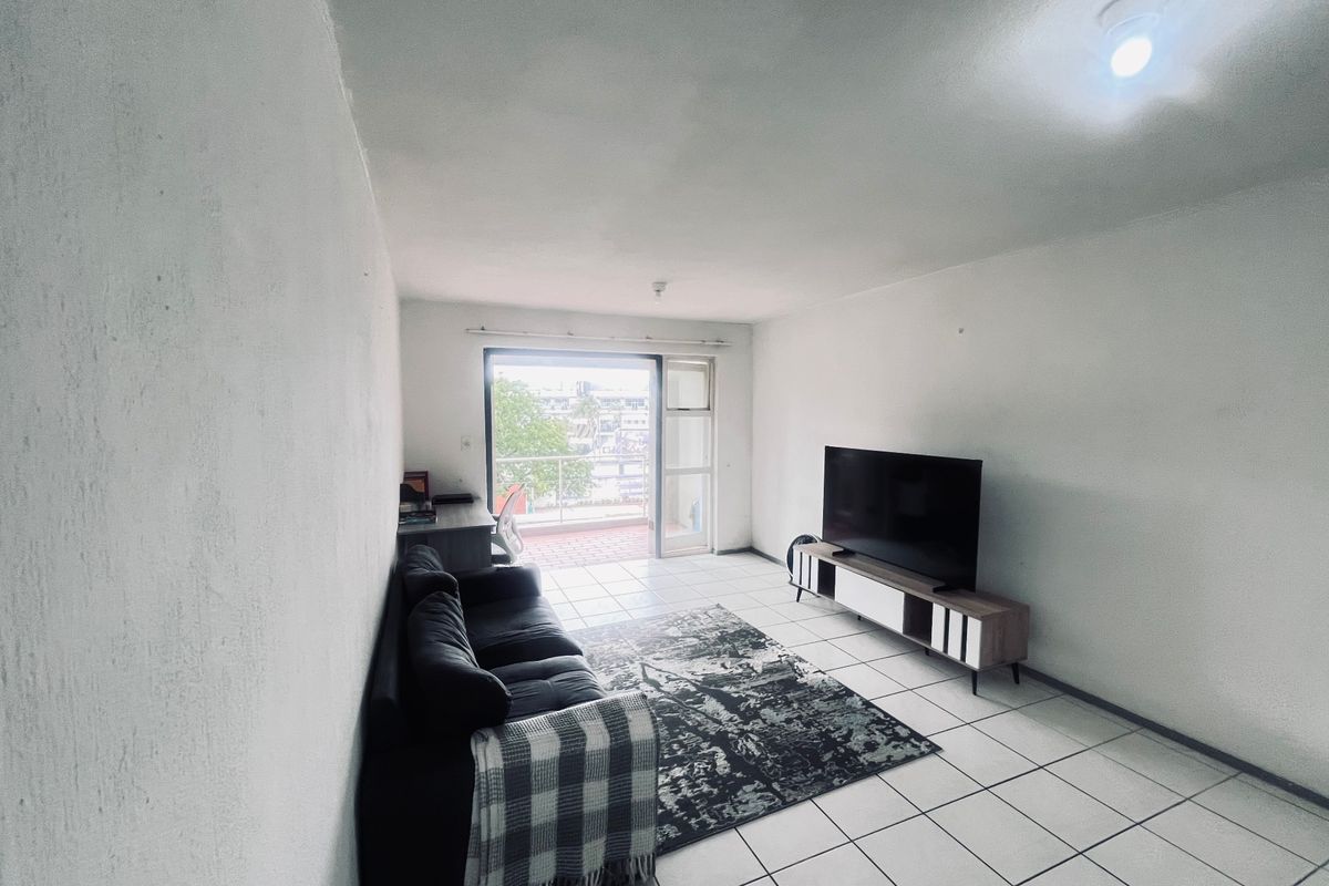 A living room featuring tiled flooring and a sliding glass door providing access to an outdoor balcony area.