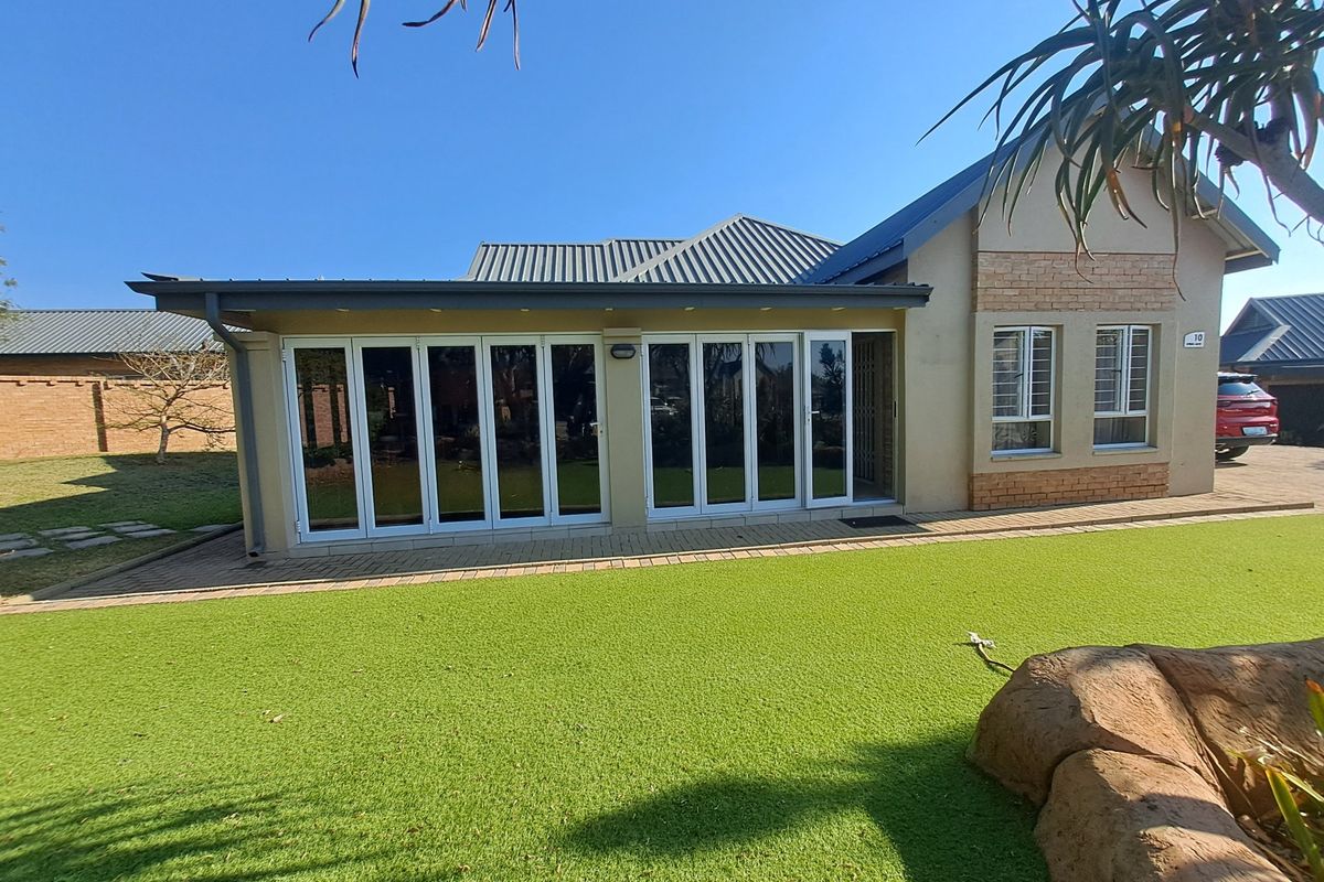 Rear view of the house featuring a paved patio, artificial lawn, and large white bi-fold doors leading into the living area.