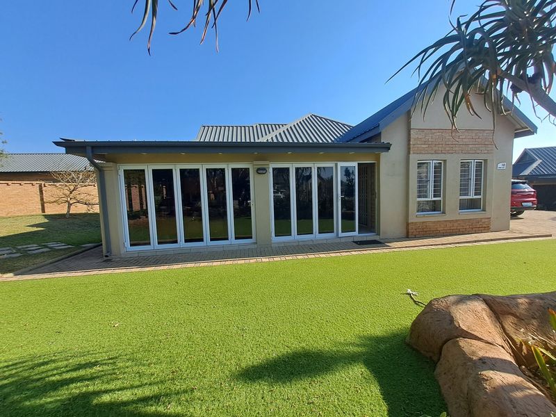 Rear view of the house featuring a paved patio, artificial lawn, and large white bi-fold doors leading into the living area.
