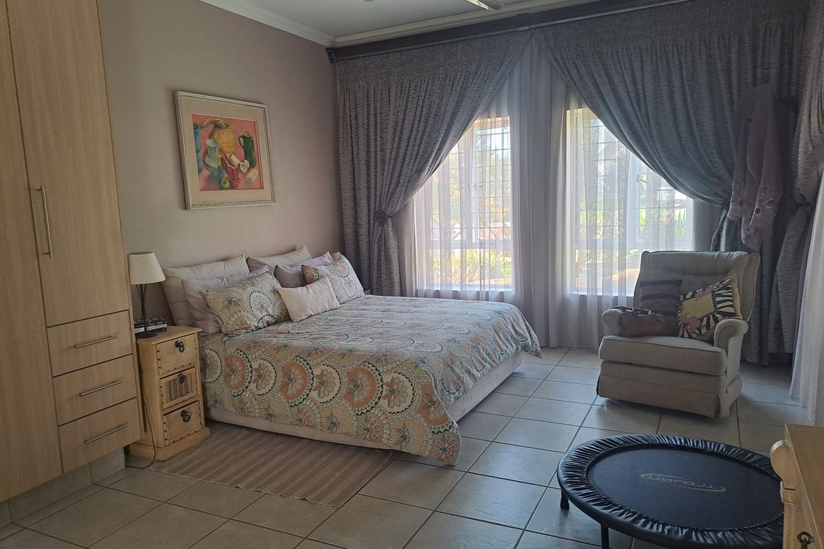 A spacious bedroom featuring tiled flooring, a built-in wardrobe, and a ceiling fan, with large windows fitted with security bars.