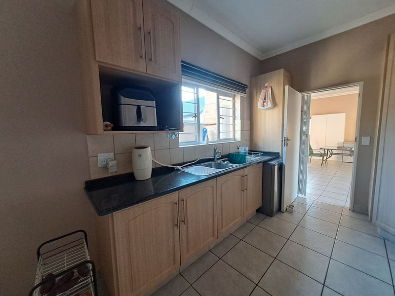 A functional kitchen featuring laminate cabinetry, granite countertops, a stainless steel sink, and tiled flooring, offering a practical workspace with natural light.