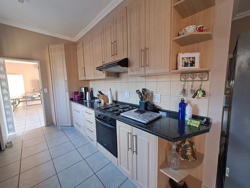 A functional kitchen featuring light wood cabinetry, granite countertops, a built-in oven, electric hob, and tiled flooring with a neutral backsplash.