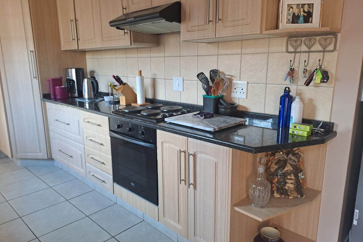 A functional kitchen featuring light wood cabinetry, granite countertops, a built-in oven, electric hob, and tiled flooring with a neutral backsplash.
