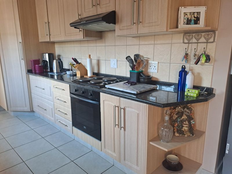 A functional kitchen featuring light wood cabinetry, granite countertops, a built-in oven, electric hob, and tiled flooring with a neutral backsplash.