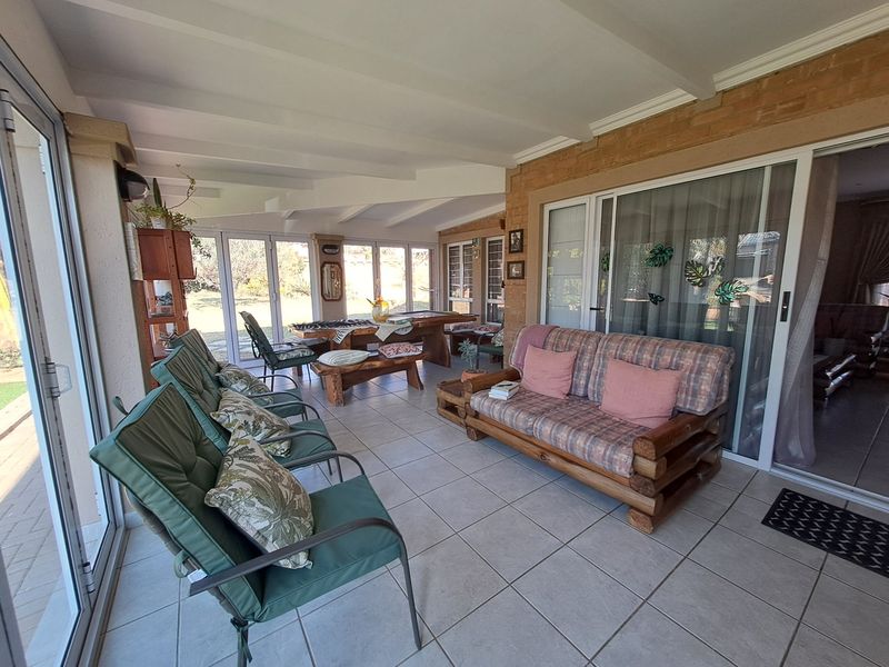 A spacious covered patio featuring tiled flooring, exposed beam ceilings, and large sliding glass doors providing seamless access to the garden area.