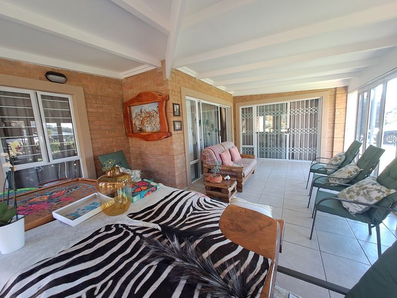 A spacious covered patio featuring exposed beam ceilings, brick wall finishes, and tiled flooring, providing a comfortable outdoor entertainment area.