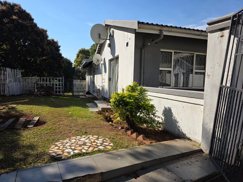Rear view of the property featuring a garden area, paved walkway, and exterior wall with sliding door access.