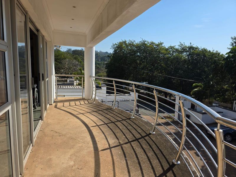 Spacious curved balcony featuring a stainless steel balustrade, sliding glass door access, and elevated views of the surrounding neighborhood.