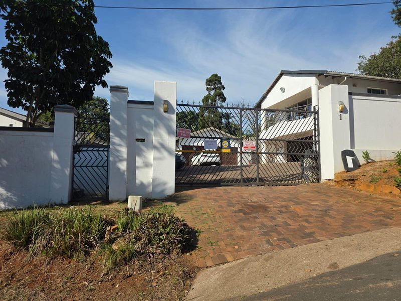 Front entrance view of the property featuring a brick driveway, secure metal gate, and masonry perimeter walling.
