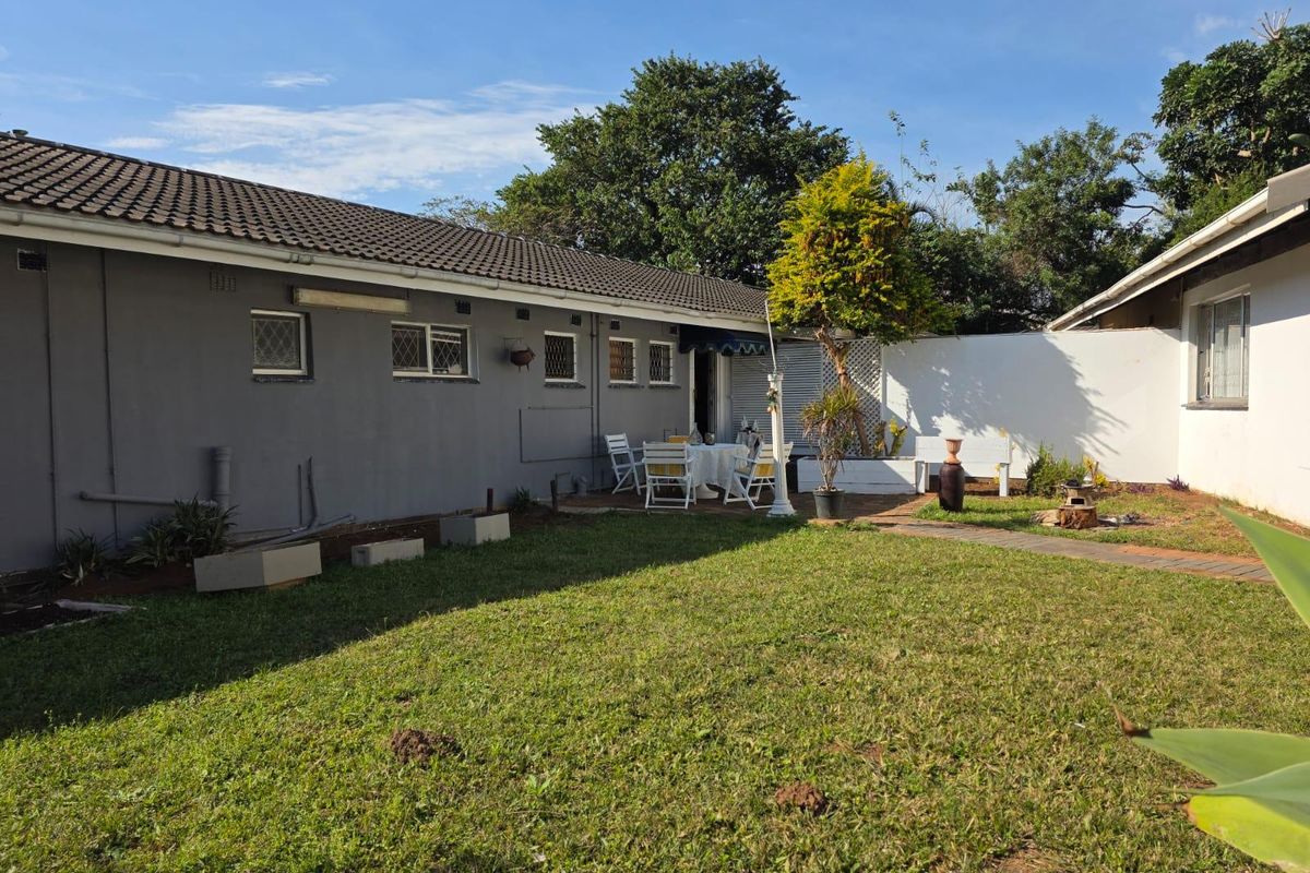 Rear view of the property featuring a paved patio area, lawn, and boundary wall, providing a private outdoor space.