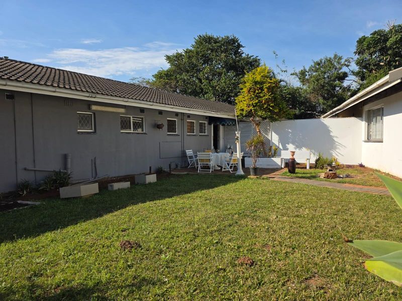 Rear view of the property featuring a paved patio area, lawn, and boundary wall, providing a private outdoor space.