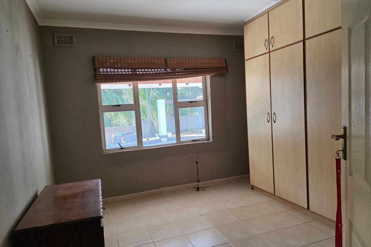 A vacant bedroom featuring tiled flooring, built-in wooden cupboards, and aluminium window frames, offering a blank canvas for potential updates.
