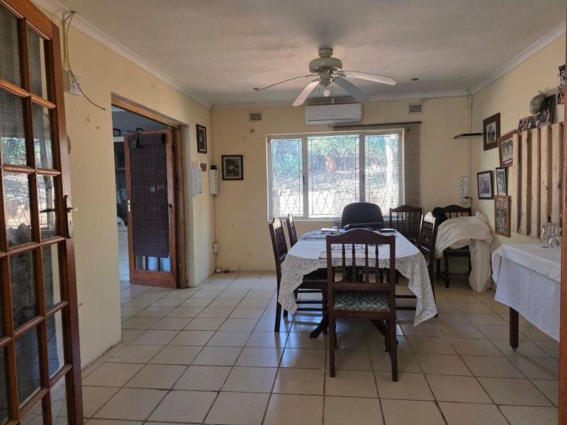 A dining room featuring ceramic tiled flooring, a ceiling fan, and a wall-mounted air conditioning unit, requiring cosmetic updates to wall finishes and flooring.