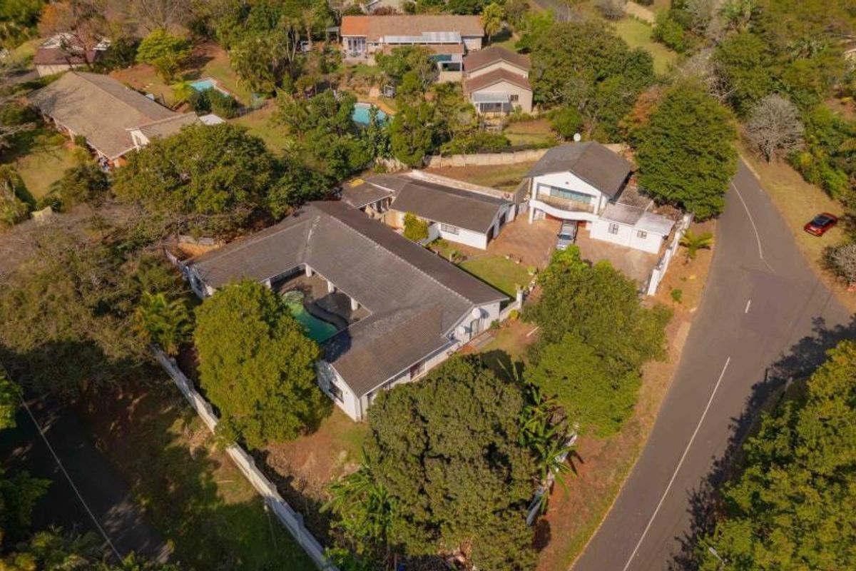 Aerial view of the property showcasing the main dwelling, swimming pool, garage, and surrounding landscaped garden area within a residential neighborhood.