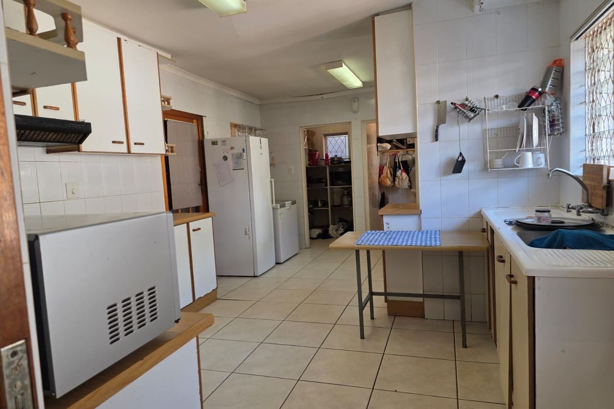 A functional kitchen featuring tiled flooring, ample built-in cabinetry, laminate countertops, and a double sink, offering potential for modern updates.