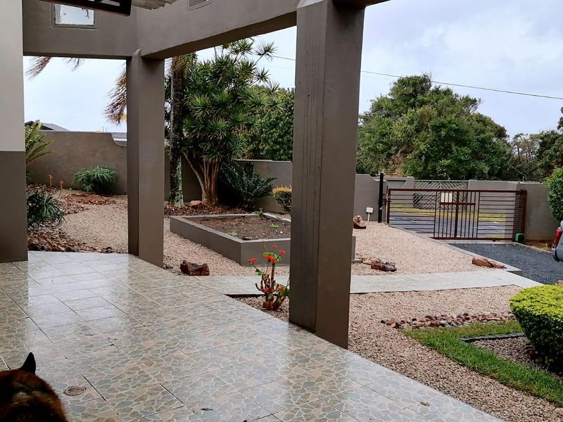 A covered patio area featuring tiled flooring and concrete pillars, overlooking a low-maintenance landscaped garden with a raised bed and secure gated entrance.
