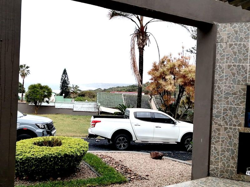 A covered patio area featuring a built-in braai with decorative stone-look tile cladding and structural concrete pillars, overlooking the garden and driveway.