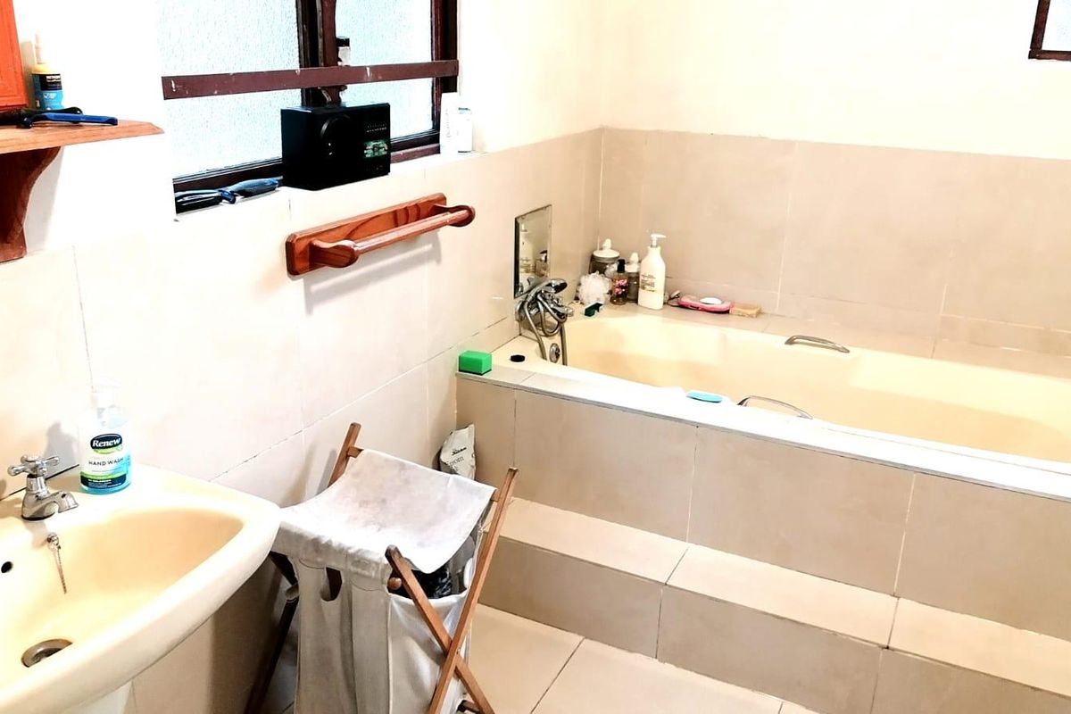 A functional bathroom featuring a built-in bathtub, wall-mounted basin, and neutral wall and floor tiling.