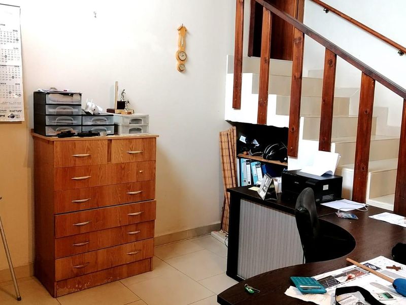 A functional home office space featuring a staircase with a wooden handrail and tiled flooring.