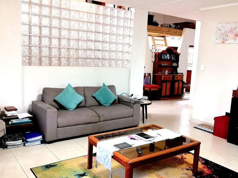 A living room featuring a distinctive glass block feature wall, tiled flooring, and an open-plan layout leading to a mezzanine level.