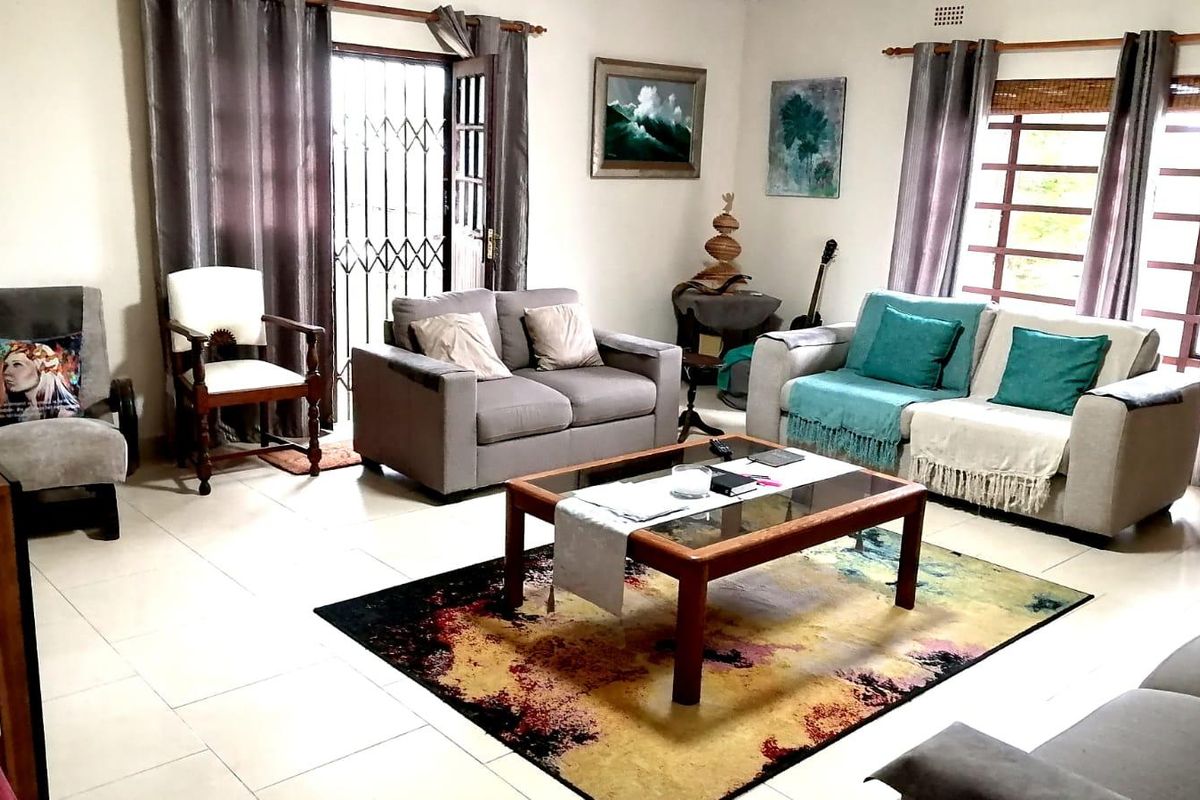 A spacious living room featuring tiled flooring, large windows with blinds, and a security gate leading to the exterior.