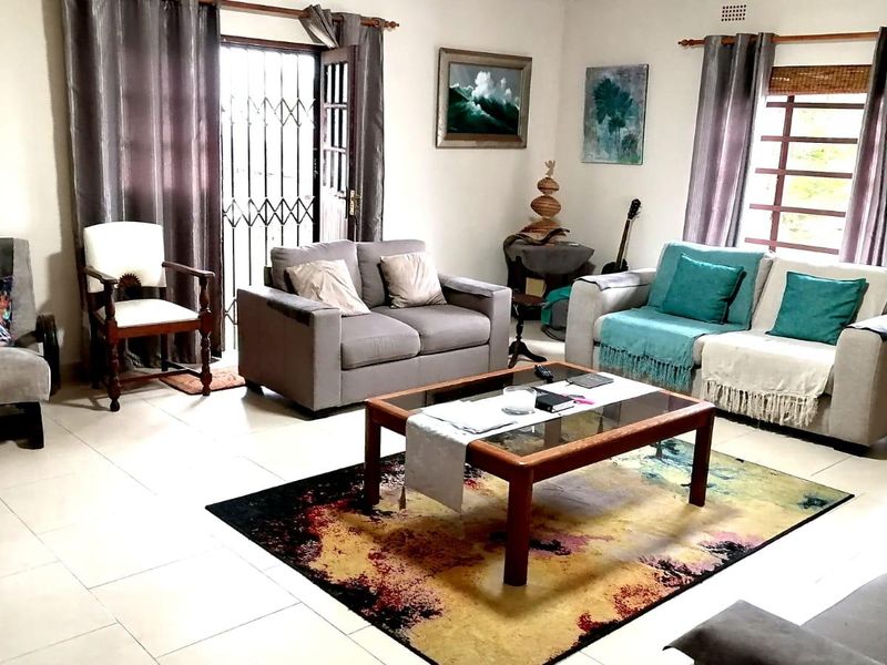 A spacious living room featuring tiled flooring, large windows with blinds, and a security gate leading to the exterior.