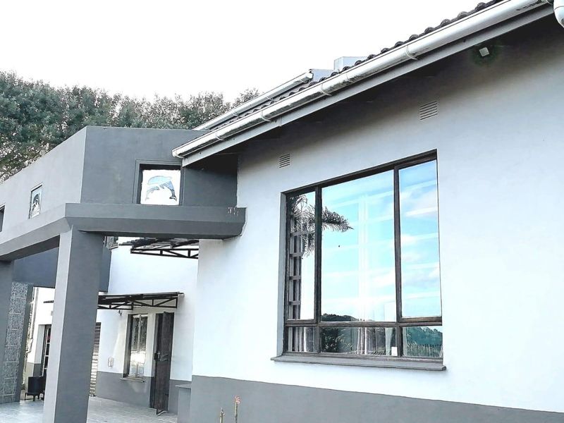 A view of the front exterior facade featuring plastered walls, aluminium window frames, and a covered entrance porch with a tiled roof.