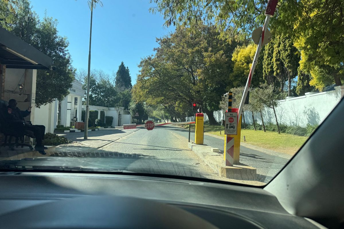 View of a secure residential estate entrance featuring a boom gate, security booth, and paved access road.
