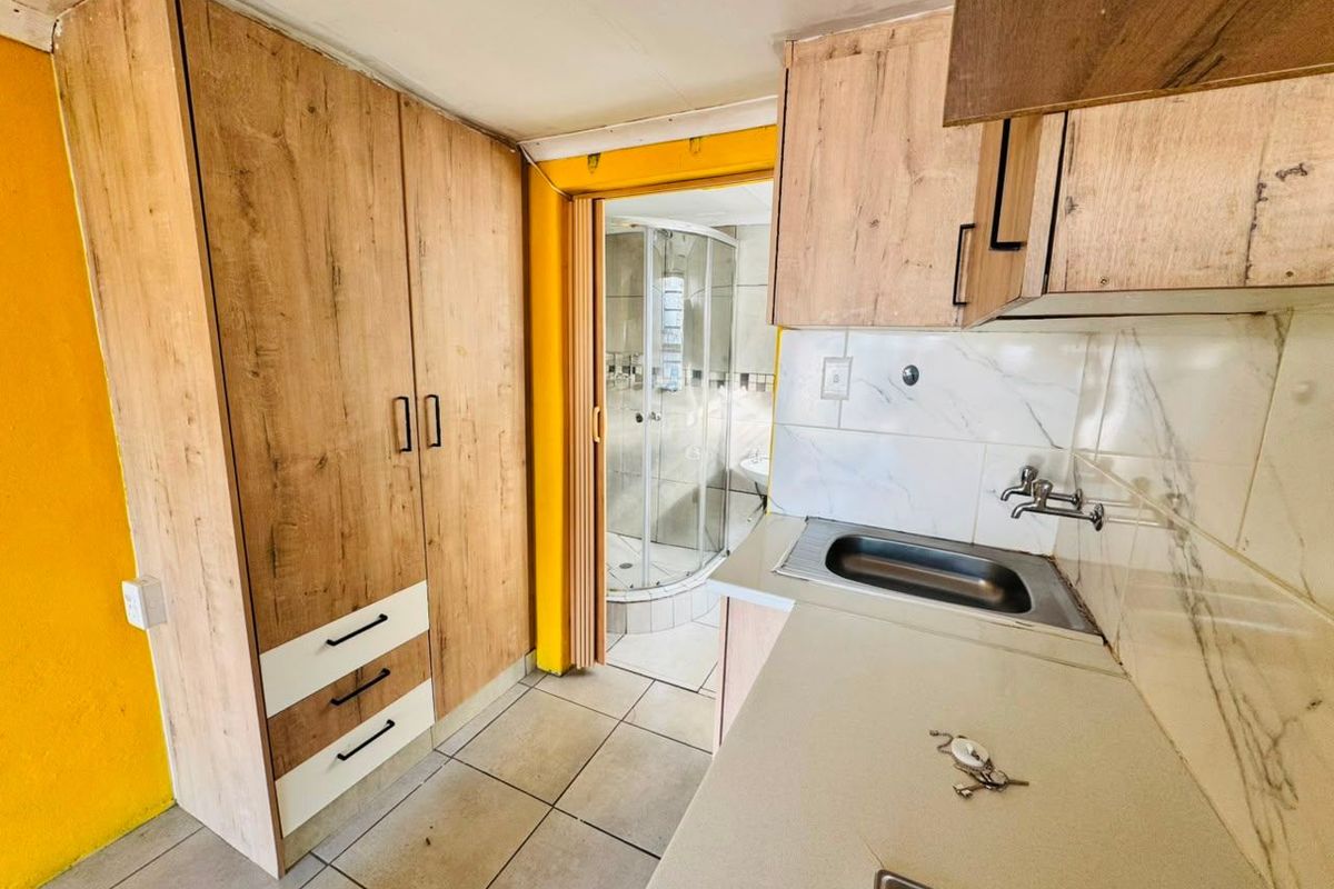 Compact kitchen area featuring built-in cabinetry and a stainless steel sink, with direct access to an adjoining bathroom with a shower enclosure.