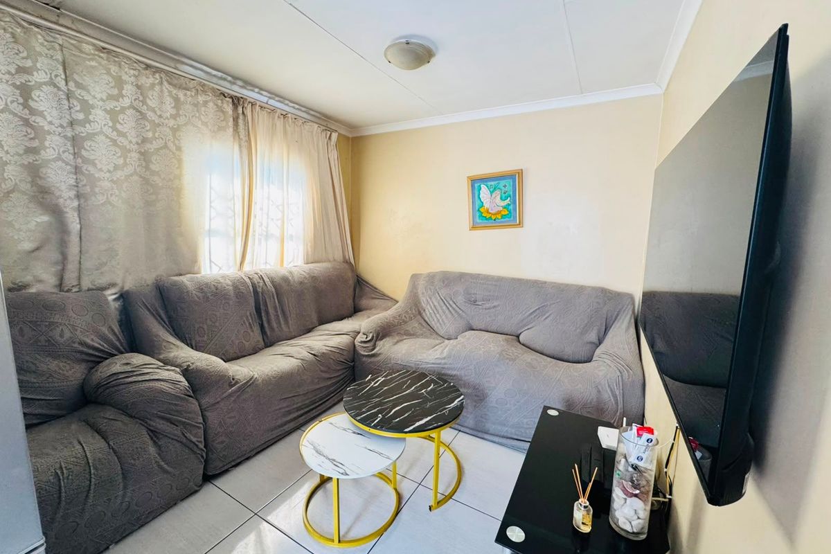 A compact living room featuring tiled flooring and standard ceiling finishes, offering a functional space that could benefit from cosmetic updates.