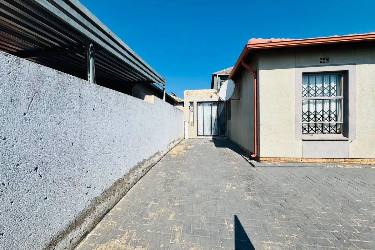 Rear exterior view showing a paved driveway, boundary wall, and carport structure adjacent to the main dwelling.