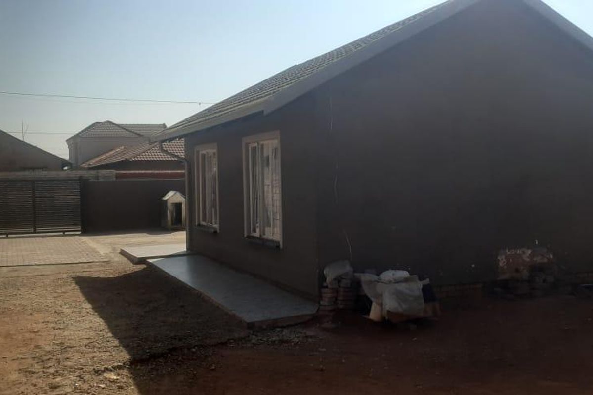 A view of the rear exterior of the house featuring plastered walls, a tiled roof, and a paved walkway leading to a gated entrance.