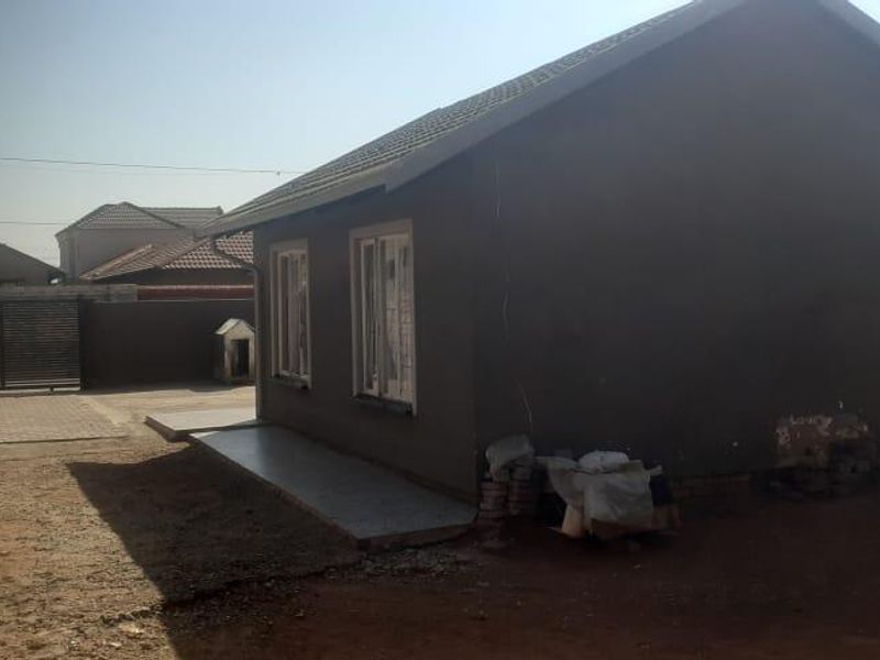 A view of the rear exterior of the house featuring plastered walls, a tiled roof, and a paved walkway leading to a gated entrance.