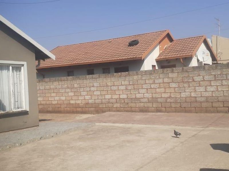 Rear exterior view of the property featuring a concrete boundary wall, paved yard area, and tiled roof structure.