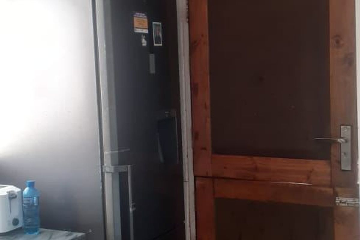 A kitchen area featuring tiled flooring, a wooden door, and ceiling detailing, currently showing signs of unfinished wall surfaces.