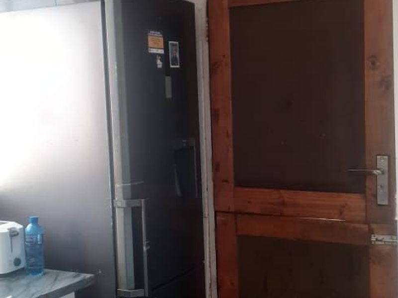 A kitchen area featuring tiled flooring, a wooden door, and ceiling detailing, currently showing signs of unfinished wall surfaces.