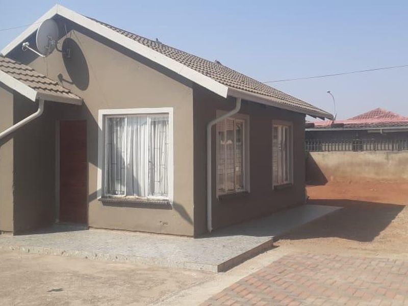 Front view of a single-story house featuring a tiled roof, paved driveway, and perimeter boundary wall in a residential setting.