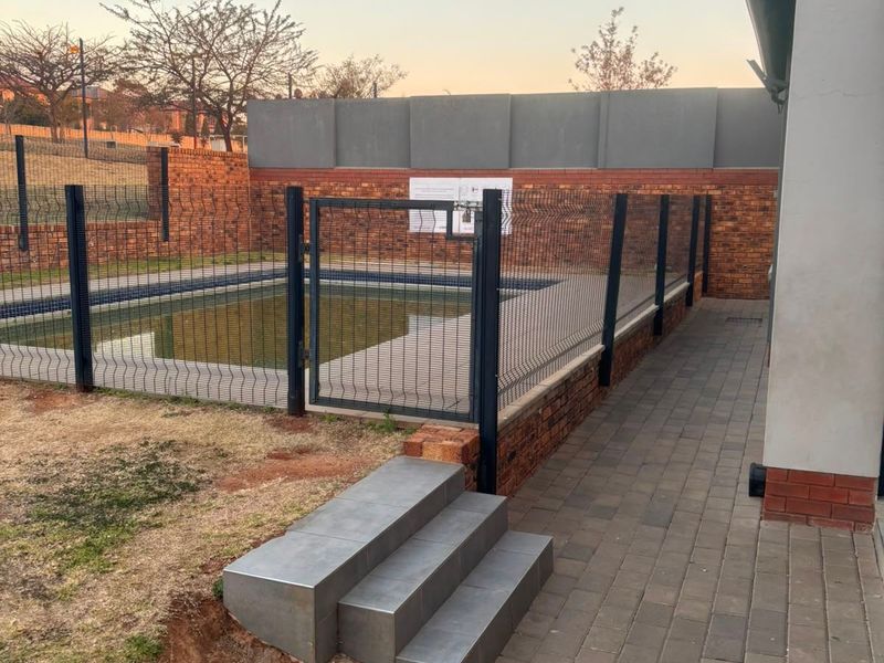 Outdoor pool area featuring a fenced swimming pool, brick boundary walls, tiled steps, and paved walkways.