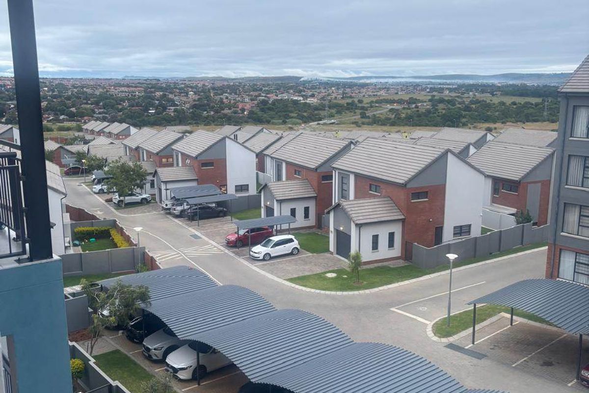 Elevated aerial view of a residential apartment complex featuring paved driveways, covered carports, and landscaped garden areas.
