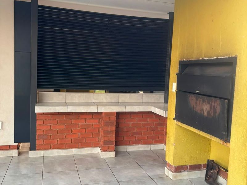 Covered patio area featuring a built-in braai, tiled flooring, and a brick-based counter with a secure metal shutter.