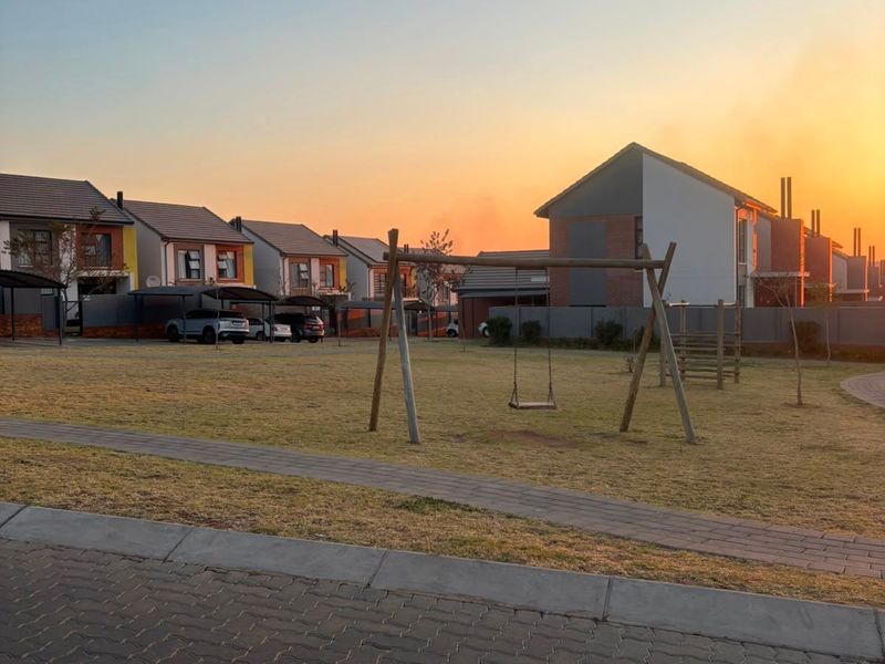 A view of a residential complex featuring paved driveways, carports, and a communal lawn area at sunset.