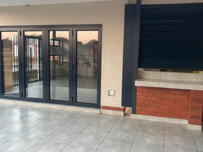 Covered patio area featuring tiled flooring, modern aluminium stacker doors, and a built-in brick braai station.
