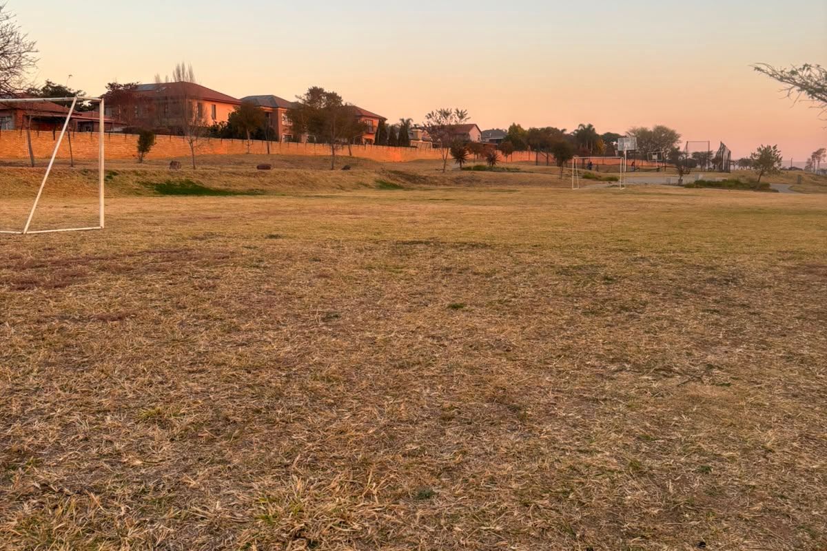 An open communal sports field featuring a soccer goal post and basketball hoop, set within a residential estate environment.