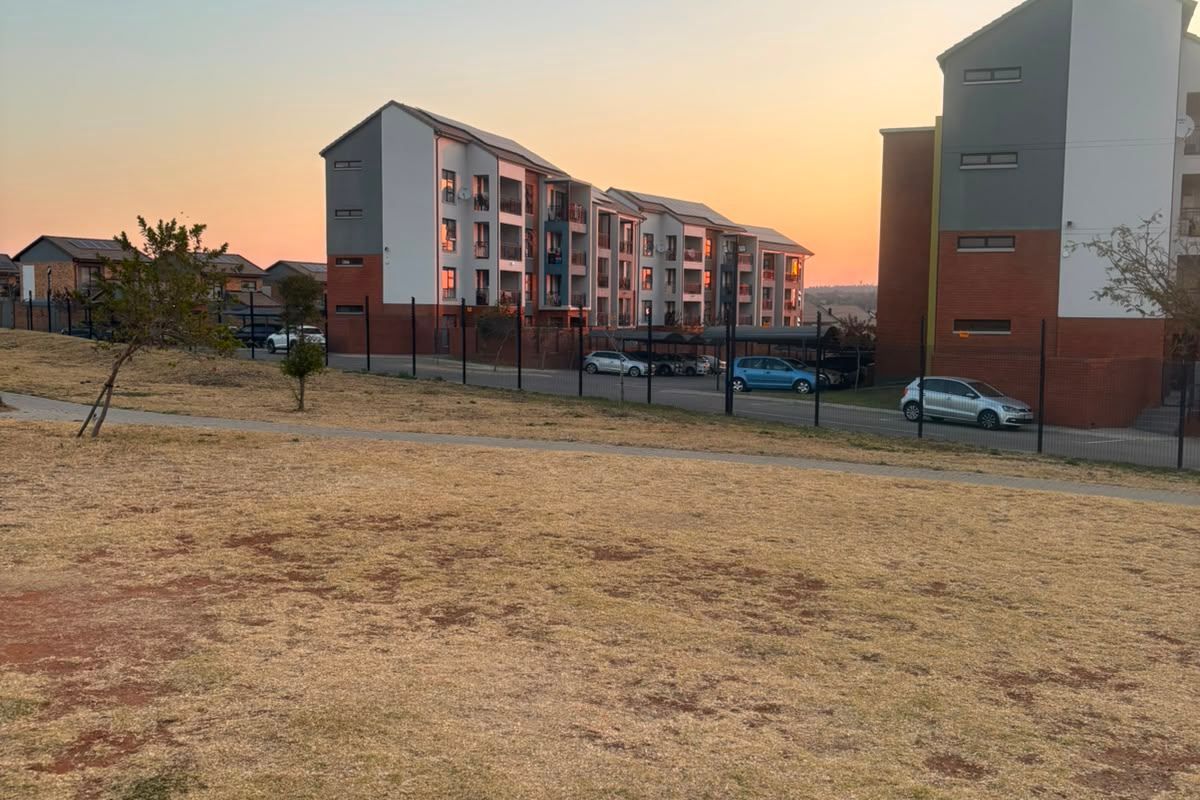 View of the apartment complex exterior, featuring multi-story residential buildings, paved parking areas, and perimeter fencing at sunset.