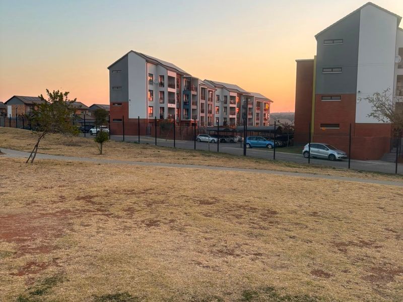 View of the apartment complex exterior, featuring multi-story residential buildings, paved parking areas, and perimeter fencing at sunset.
