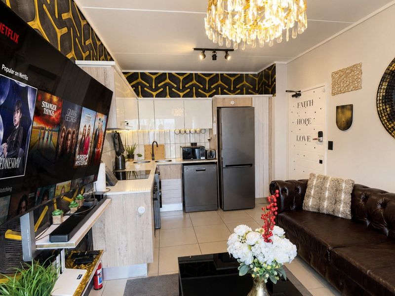 A compact open-plan living and kitchen area featuring modern cabinetry, tiled flooring, and a contemporary chandelier, creating a functional and stylish apartment space.