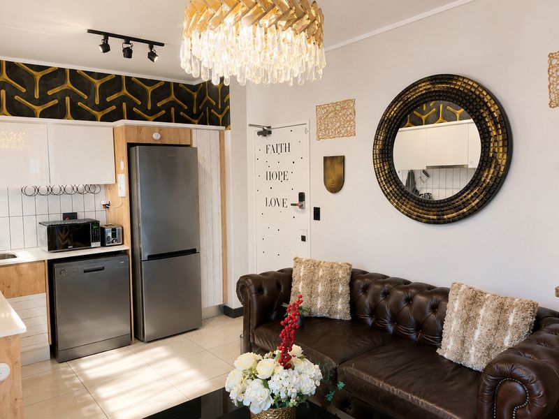 Modern open-plan living area featuring a compact kitchen with stainless steel appliances, tiled flooring, and contemporary lighting fixtures.