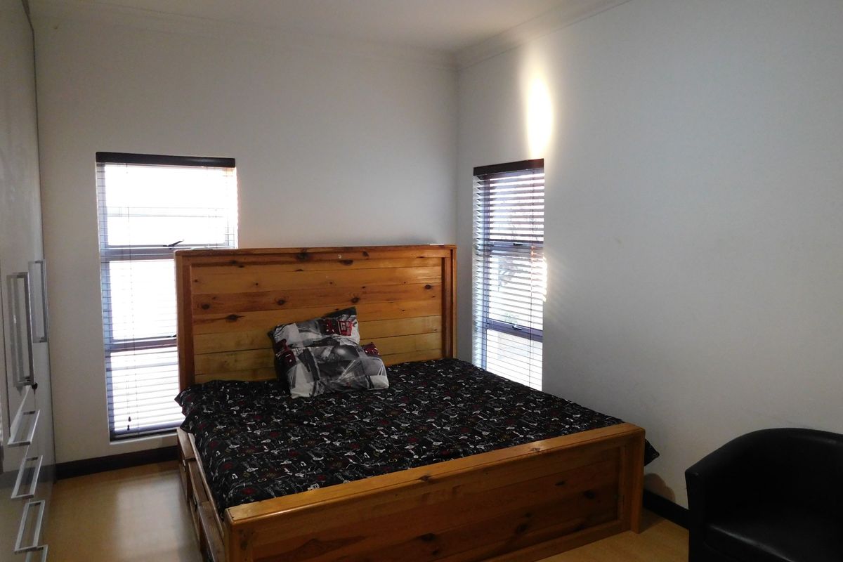 A functional bedroom featuring laminate flooring, built-in wardrobe storage, and dual windows fitted with venetian blinds.