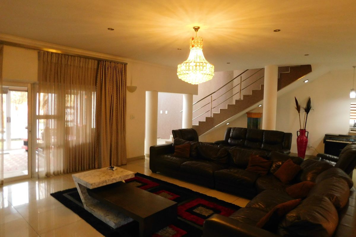 Spacious living room featuring tiled floors, a prominent crystal chandelier, and an open staircase with a modern metal balustrade.