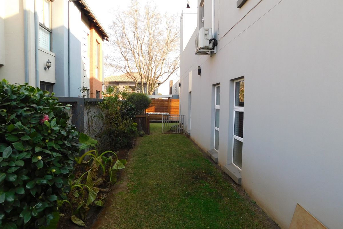 A side garden pathway featuring a manicured lawn, boundary wall, and external wall-mounted air conditioning unit.